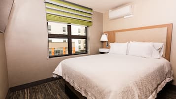 A hotel room with a large bed, a window with striped curtains, a bedside table with a lamp, and an air conditioning unit on the wall.
