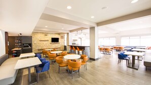 A spacious indoor dining area with multiple tables and chairs, a stone accent wall, and a television screen. - Hampton Inn & Suites Seattle-Downtown (Seattle)