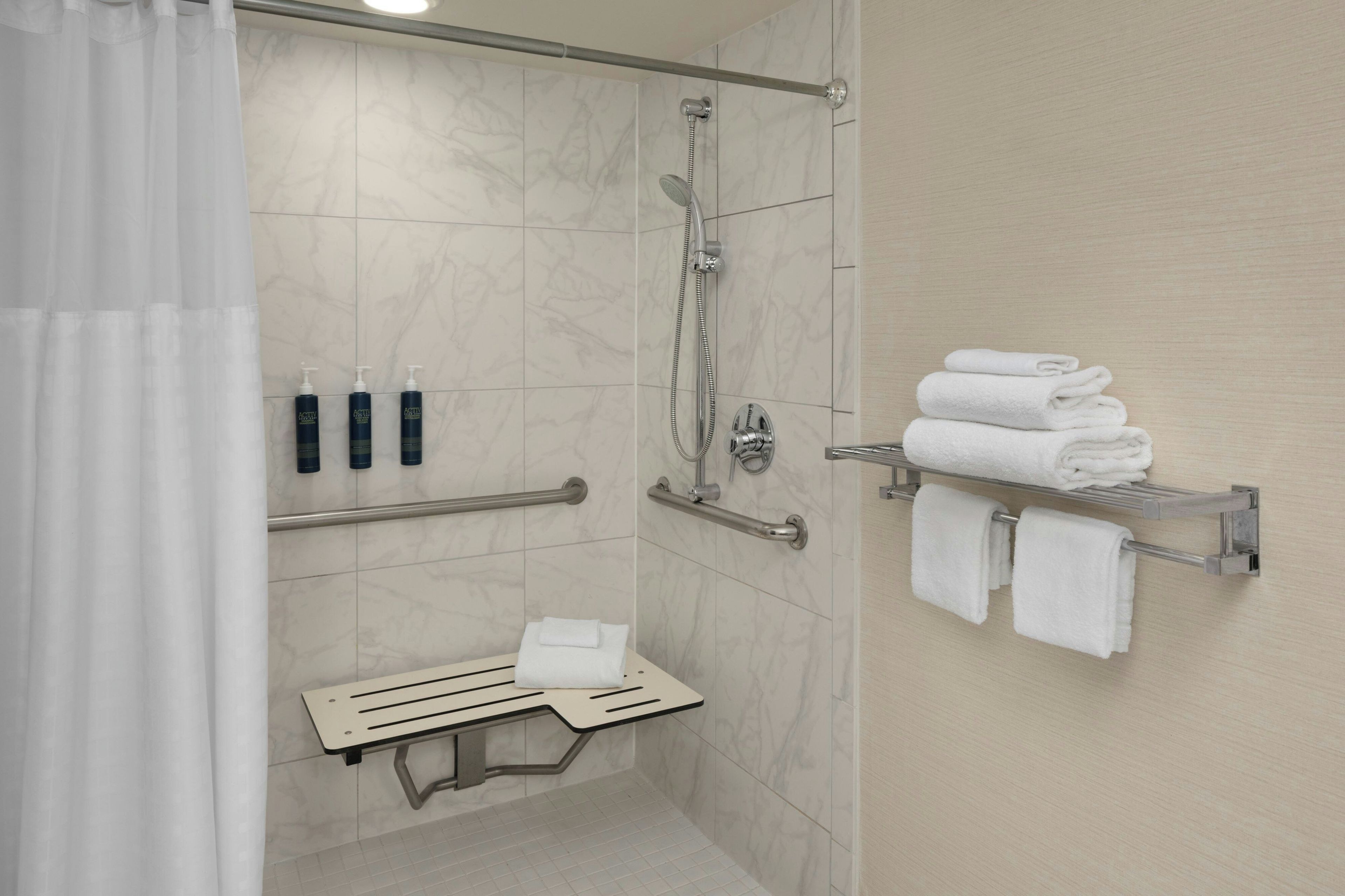 Un baño moderno con ducha, barras de apoyo, un perchero y un banco.