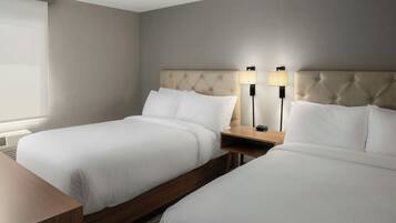 Une chambre d’hôtel avec deux lits, une table de chevet en bois et une lampe fixée au mur.