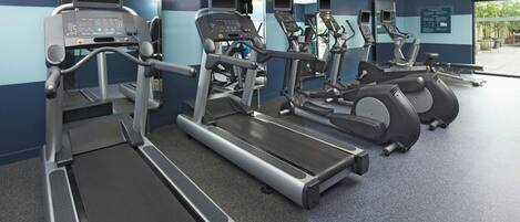 A gym with treadmills, ellipticals, and a mirrored wall.