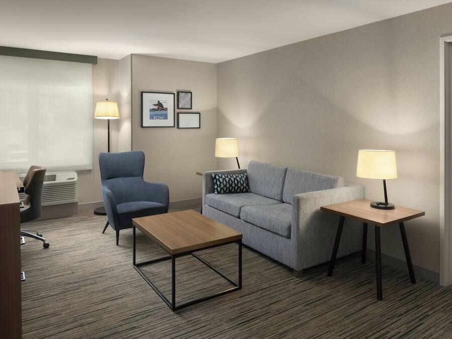 Habitación de hotel con escritorio, dos sillones, un sofá, una mesita de centro, dos mesitas de noche con lámparas y una cama.