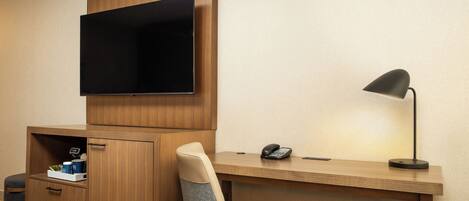 A hotel room with a wooden desk, a chair, a television mounted above the desk, a telephone, and a lamp.