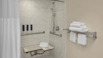 Une salle de bain moderne équipée d’une douche, de barres d’appui, d’un banc et d’un porte-serviettes.