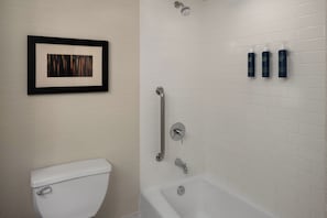 A bathroom with a white toilet, a framed artwork, a shower with a grab bar, and three bottles of toiletries on the wall. - Four Points by Sheraton Downtown Seattle Center (Seattle)
