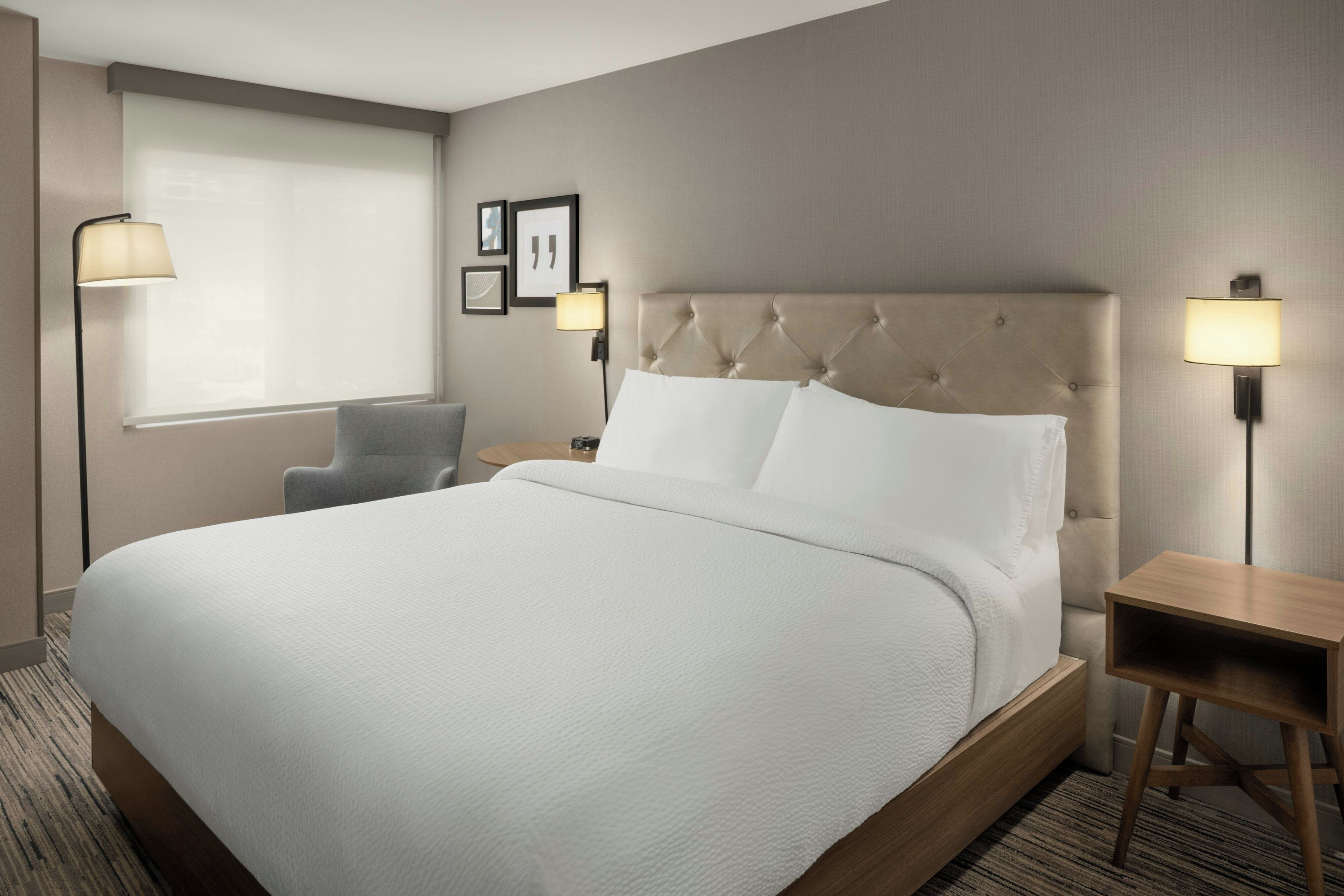 A hotel room with a large bed, a chair, a bedside table, and a lamp.