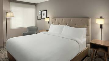 A hotel room with a large bed, a chair, a bedside table, and a lamp.