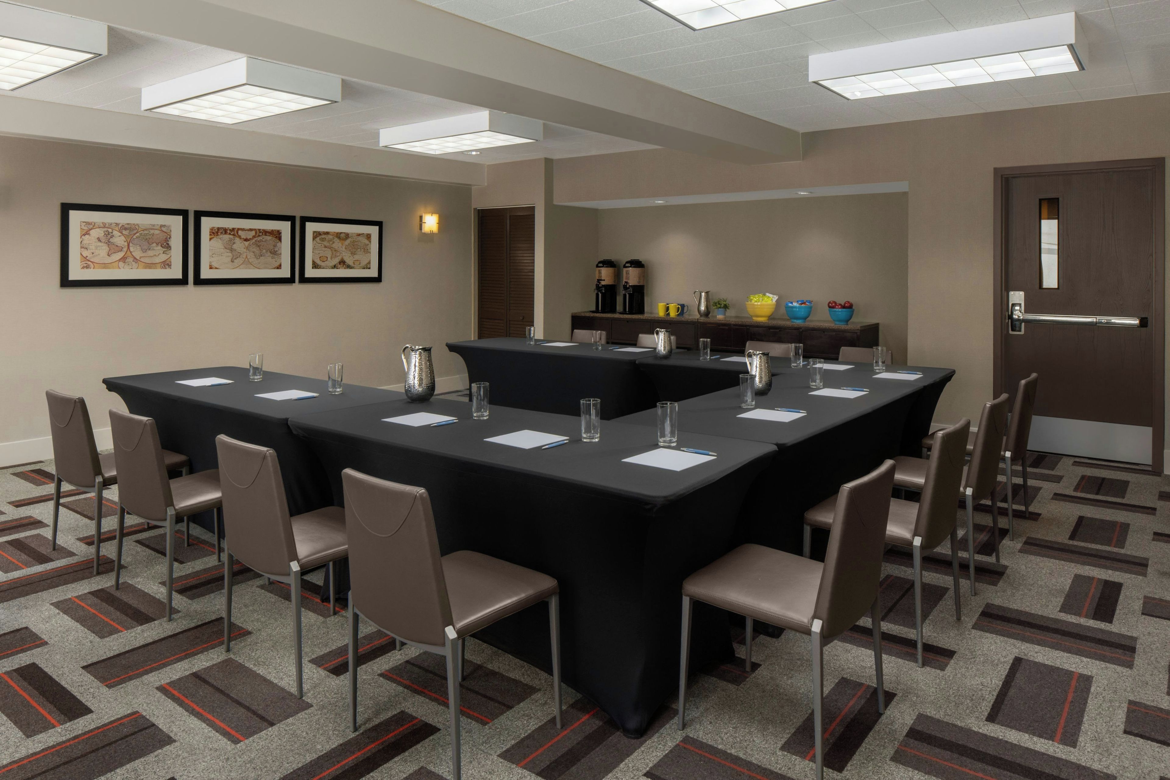 A conference room with a large table, chairs, a coffee station, and framed artwork on the wall.