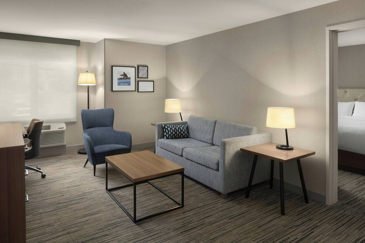 Habitación de hotel con escritorio, dos sillas, sofá, dos mesitas de noche con lámparas, cama y piso alfombrado.