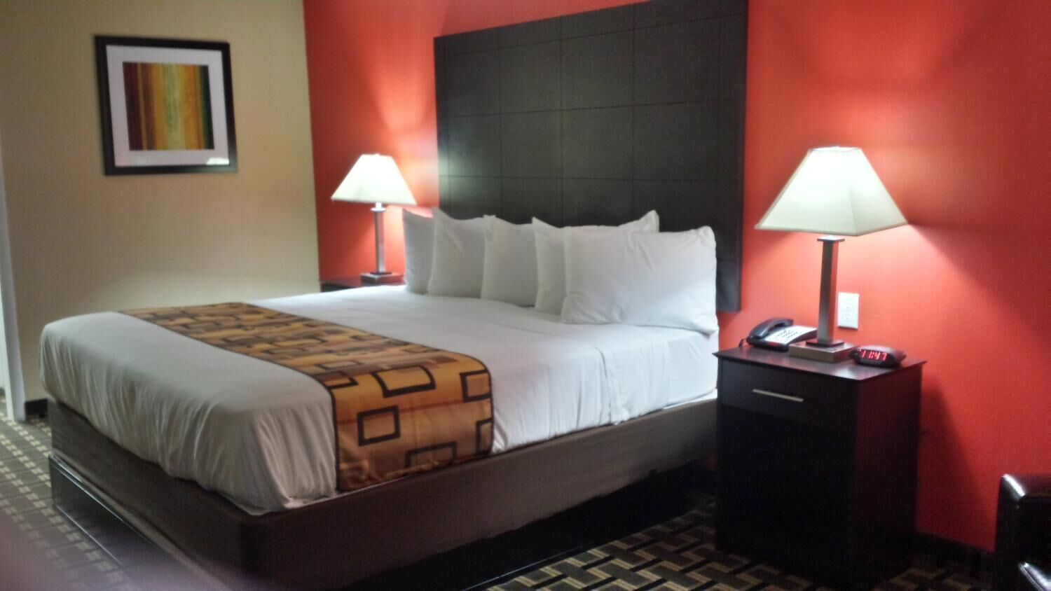 A hotel room with a large bed, two bedside tables, a red accent wall, and a patterned throw blanket.