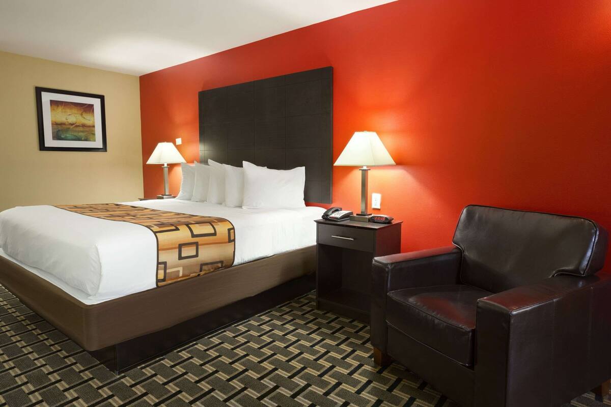 A hotel room with a bed, two bedside tables with lamps, a chair, and a large headboard.