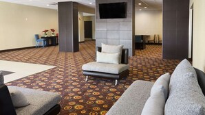 Eine Lobby mit Teppichmuster, einer Couch, einem Sessel und einem an der Wand befestigten Fernseher.