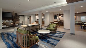 A spacious hotel lobby with a modern design, featuring a seating area with sofas and chairs, a central coffee table, and a large rug with a blue abstract pattern. - Fairfield by Marriott Inn & Suites Seattle Sea-Tac Airport (SeaTac)