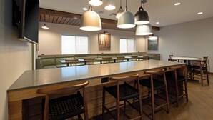 A modern bar area with a long counter, multiple bar stools, and pendant lighting. - Fairfield by Marriott Inn & Suites Seattle Sea-Tac Airport (SeaTac)