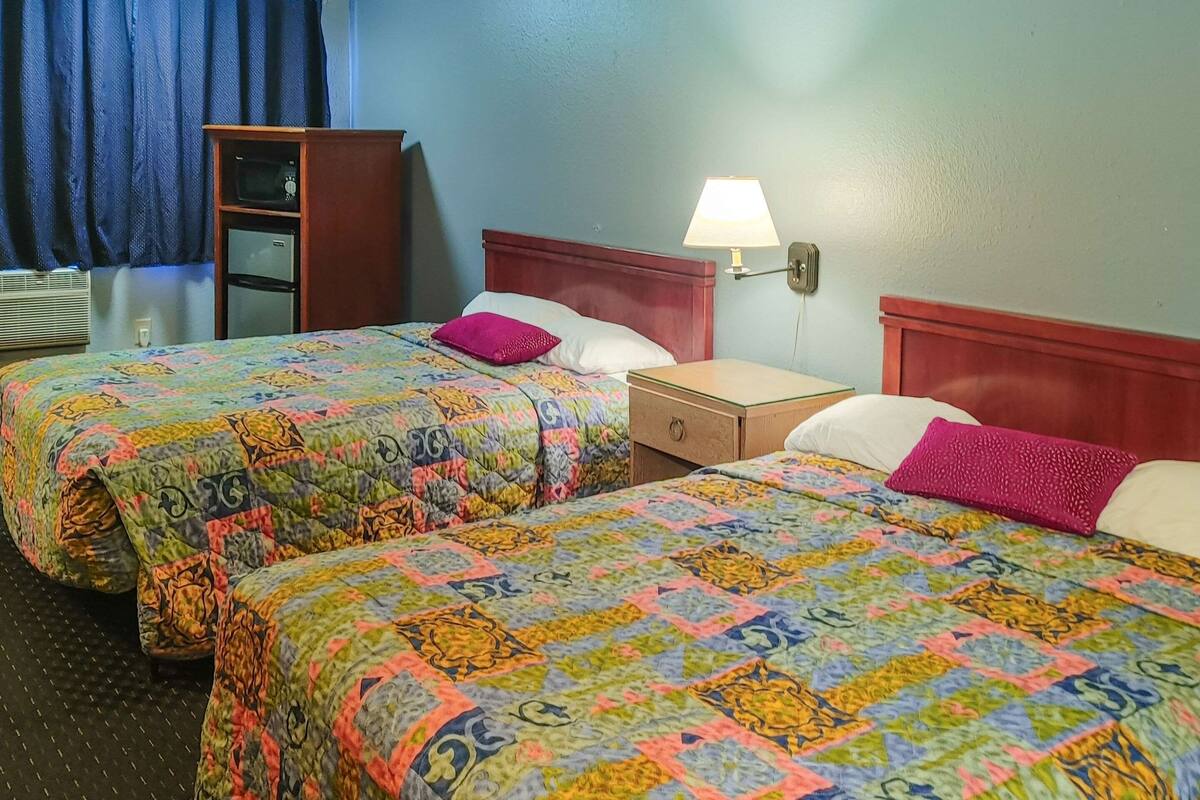 Ein Hotelzimmer mit zwei Betten, jedes mit farbenfrohen Quilts, einem Nachttisch, einer Lampe und einem kleinen Holzschrank.