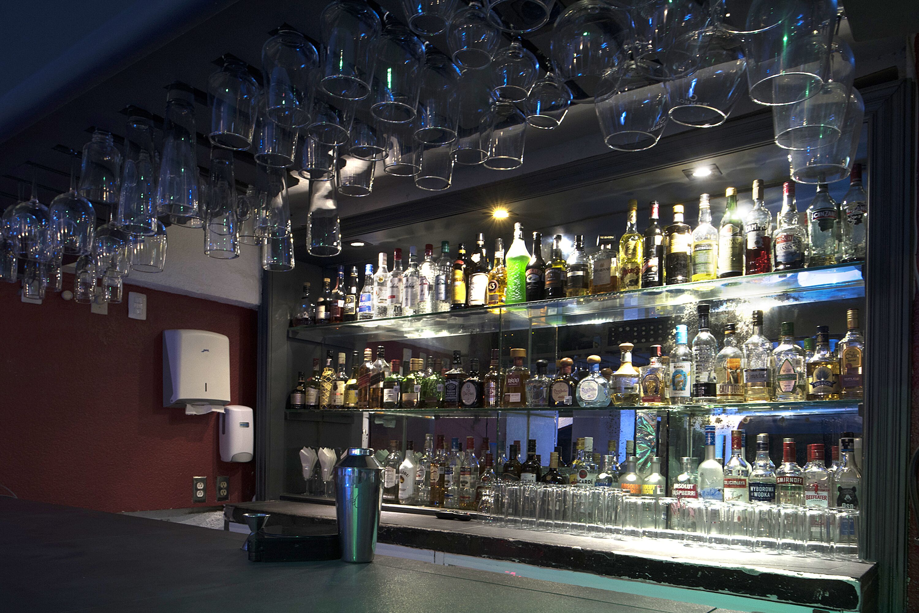 A bar with multiple shelves of liquor bottles and a large number of hanging glasses.