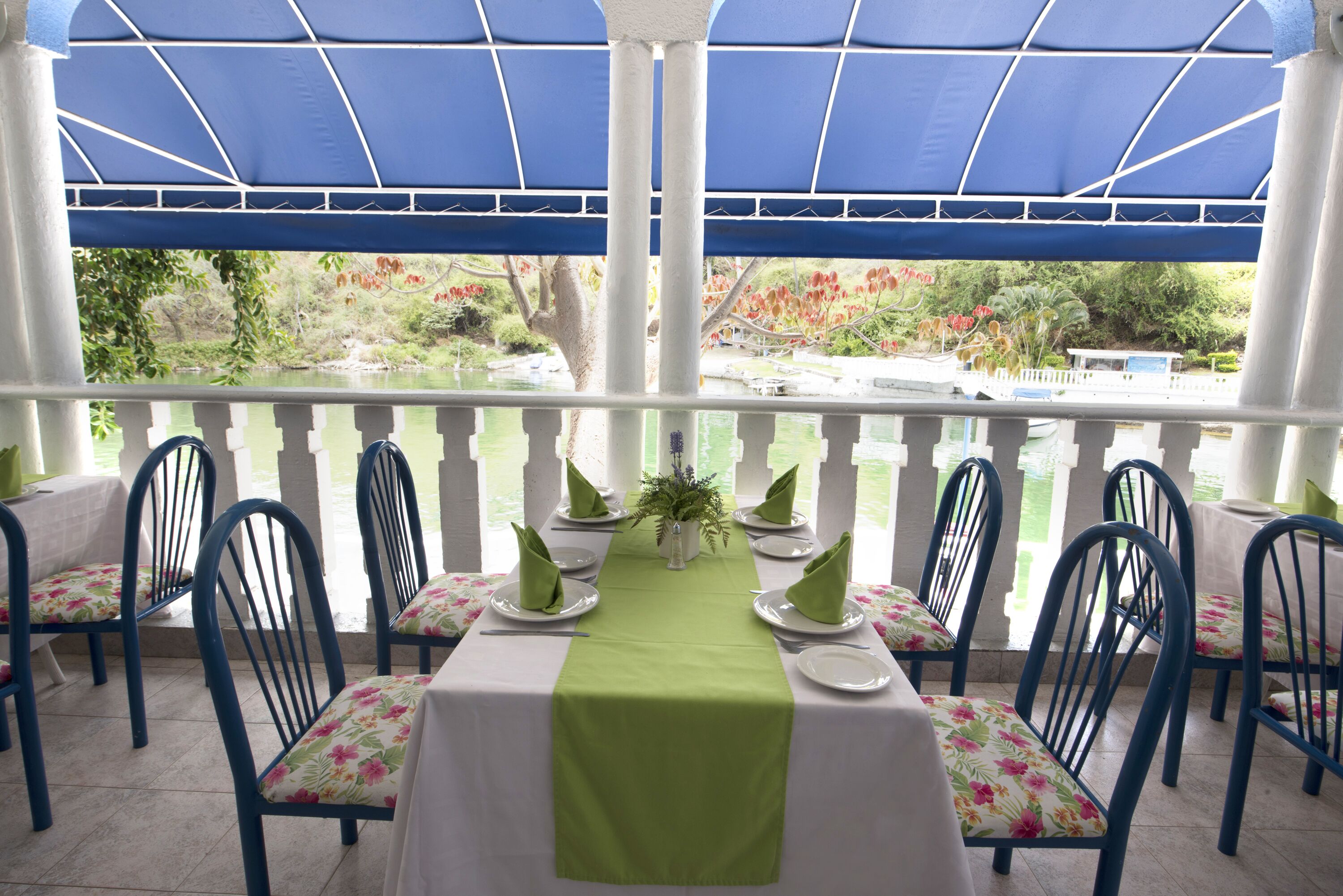 A covered outdoor dining area with a table set for six, surrounded by chairs with floral cushions.