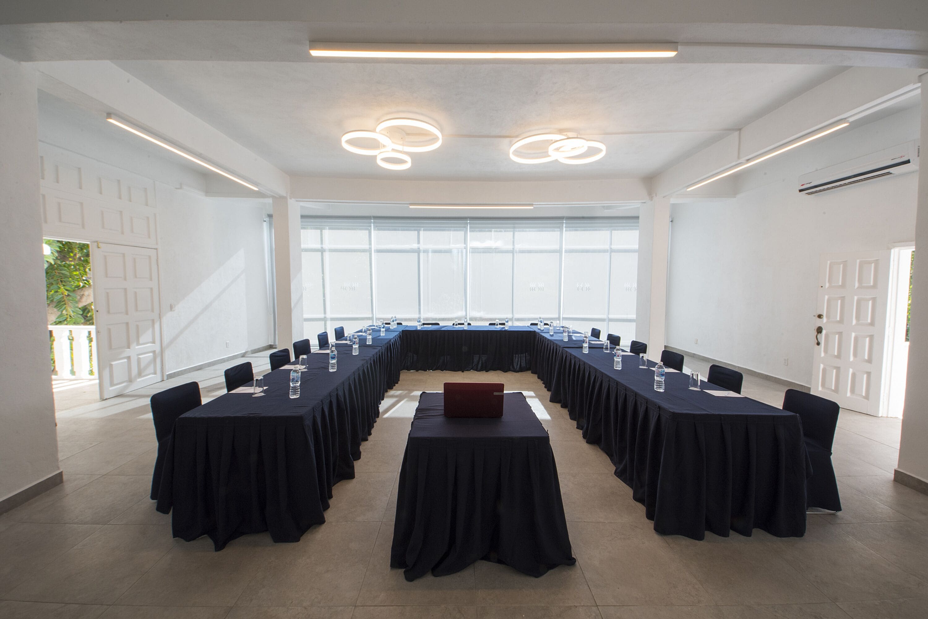 Un salón de conferencias con una larga mesa, sillas y una computadora portátil.