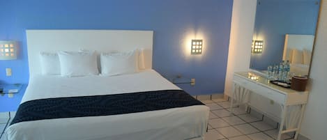 Et hotelværelse med en stor seng, et natbord, et spejl og en vægmonteret aircondition.