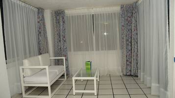 A room with a white sofa, a glass coffee table, and a window with sheer curtains.