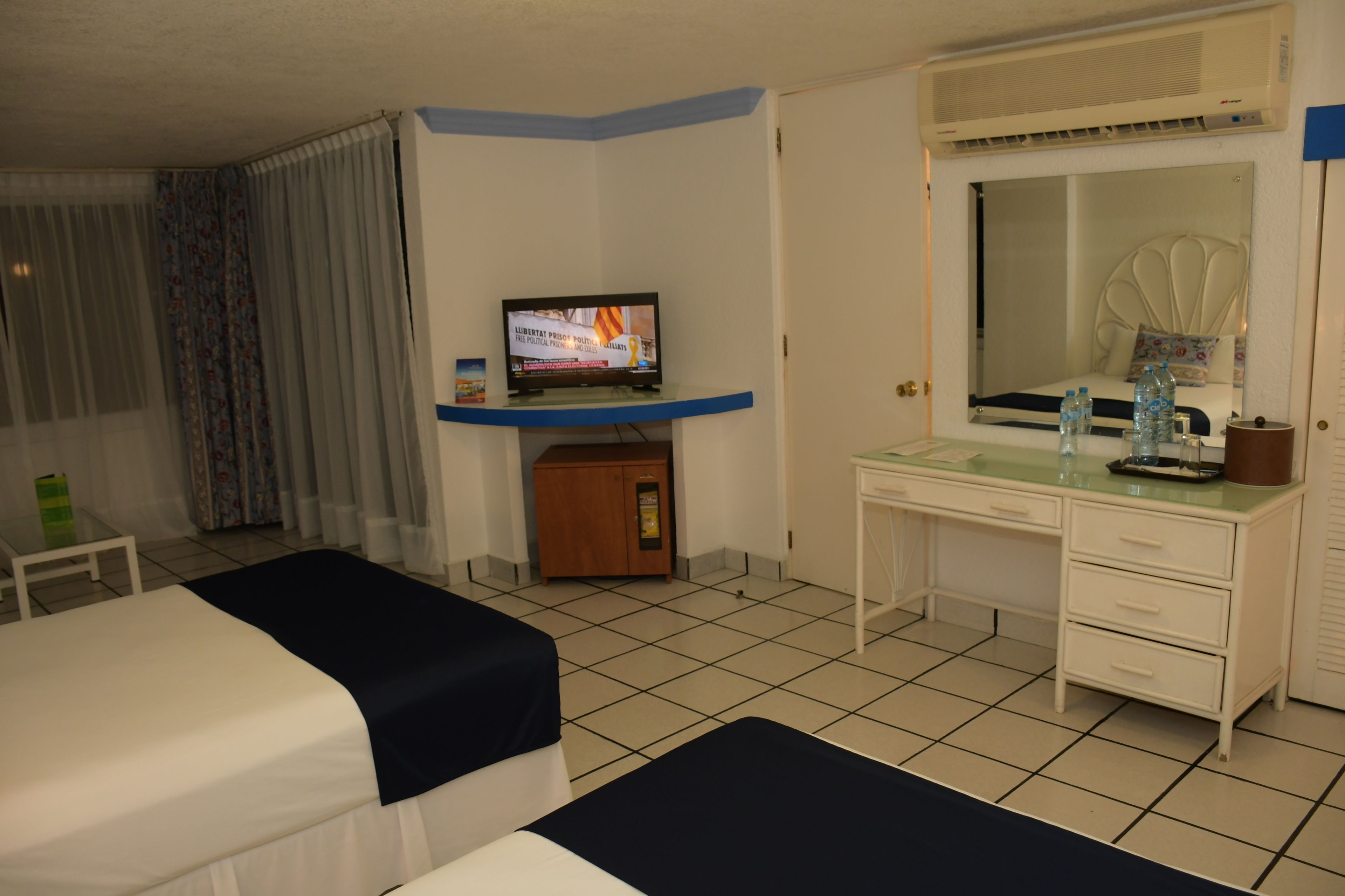 Une chambre d’hôtel avec deux lits, un bureau, une télévision et un miroir.