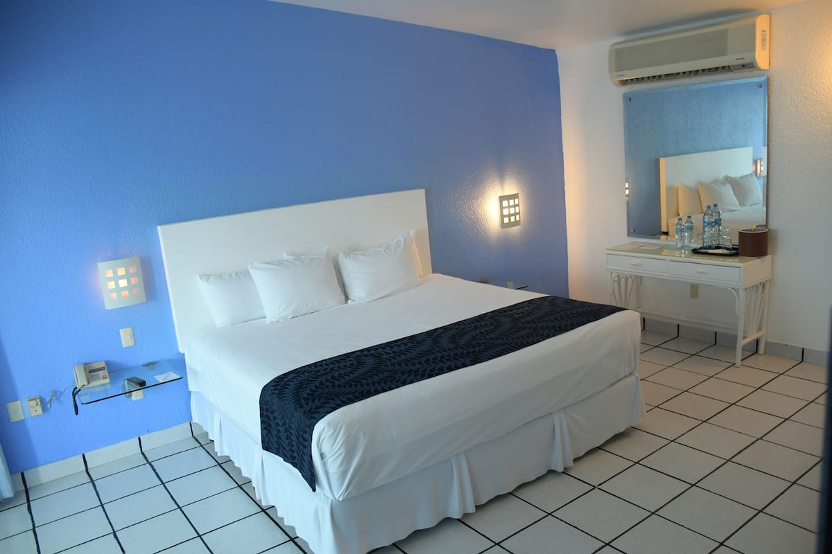 A hotel room with a bed, a bedside table, a mirror, and a wall-mounted air conditioner.
