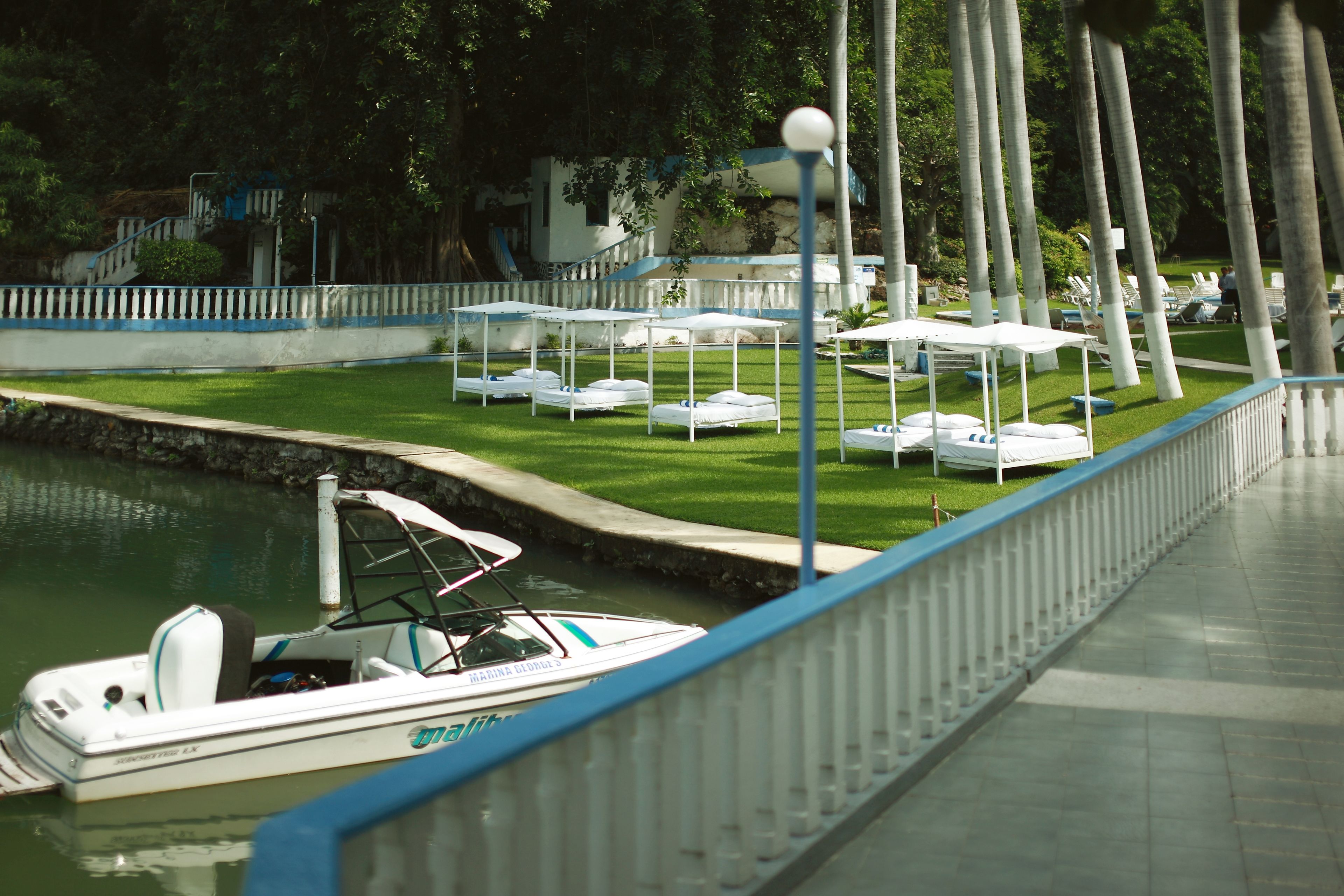 Una marina con barche ormeggiate, una zona verde con ombrelloni e un percorso lungo l'acqua.