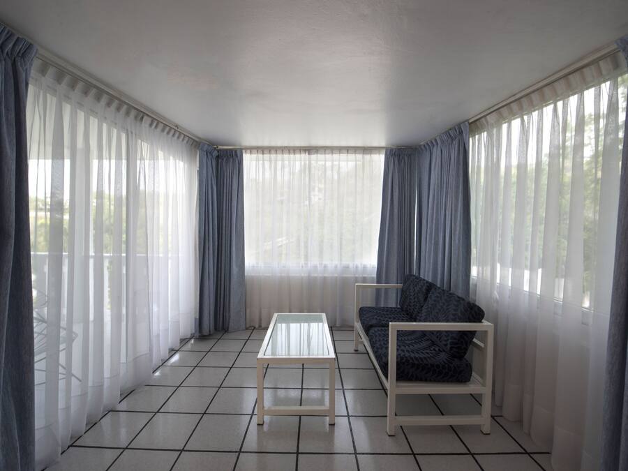 Una habitación con sofá, una mesita y cortinas ligeras.