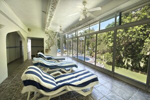 Una habitación soleada con ventiladores de techo, ventanas grandes y toallas a rayas en sillones de descanso.