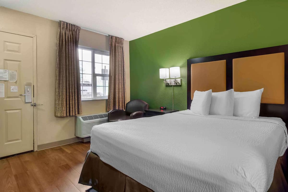 A hotel room with a large bed, a desk, a chair, a window with curtains, and a green wall.