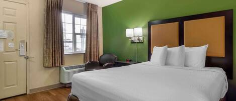 A hotel room with a large bed, a desk, a chair, a window with curtains, and a green wall.