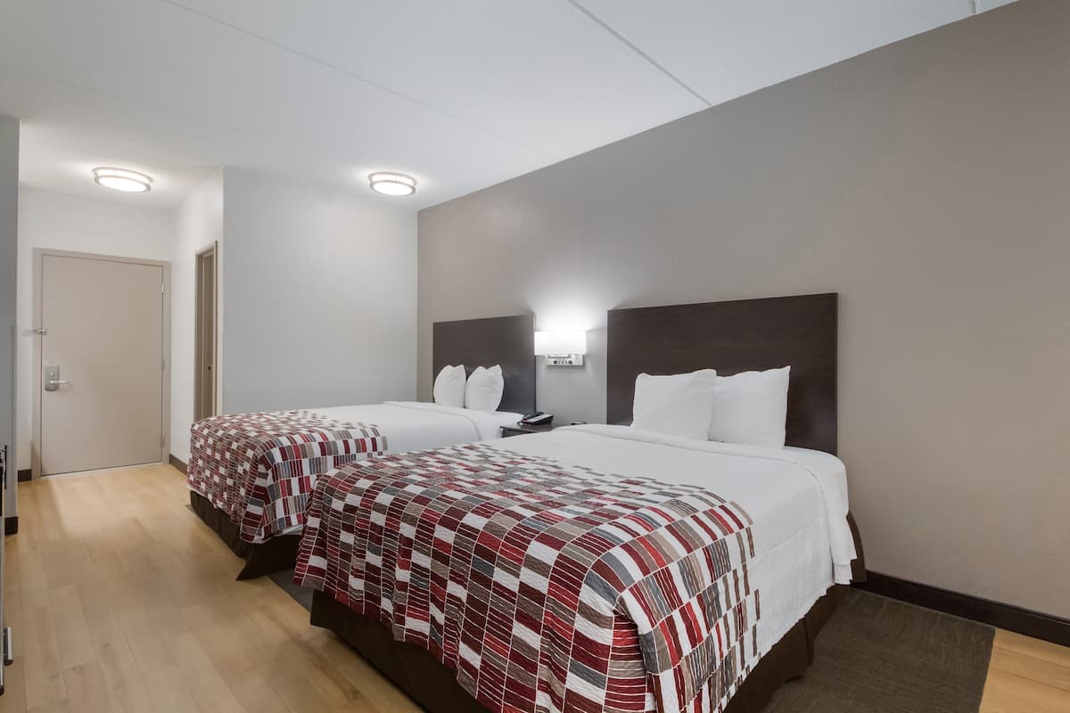 Une chambre d’hôtel avec deux lits, chacun recouvert d’une couvre-lit à carreaux rouges et blancs, doté d’une tête de lit sombre et agrémentée d’une table de chevet avec une lampe.