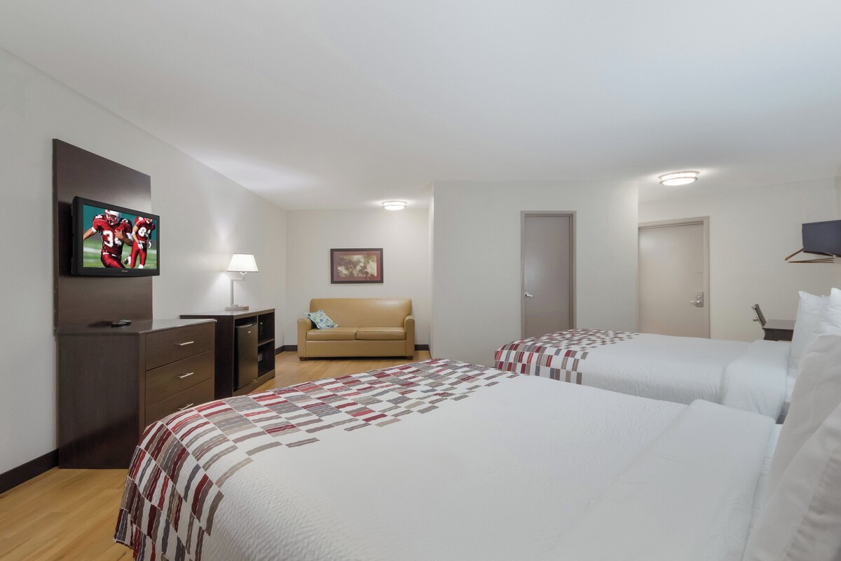 A hotel room with two beds, a TV, a sofa, and a desk.