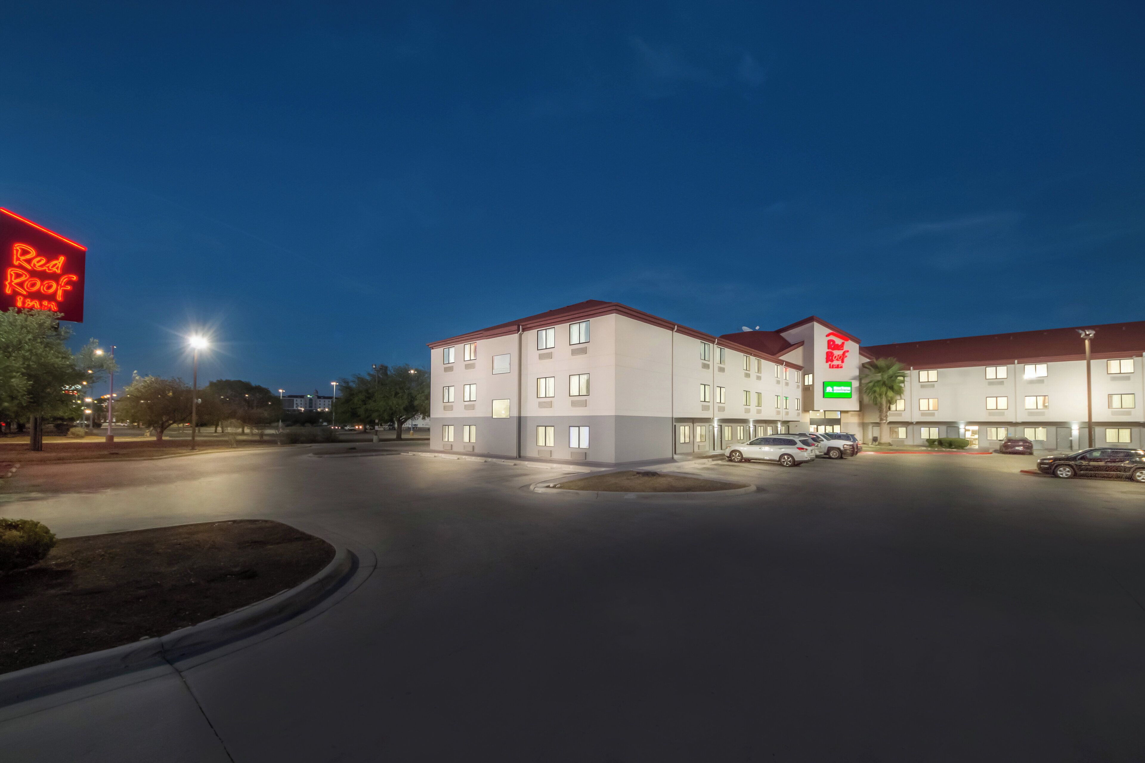 Un hotel dal design moderno, con diversi piani e un'area parcheggio con diverse auto.