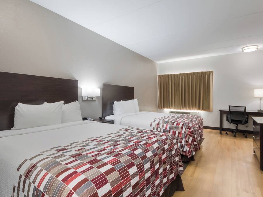 Quarto de hotel com três camas, uma mesa e um espelho.