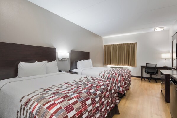 A hotel room with three beds, a desk, and a mirror.