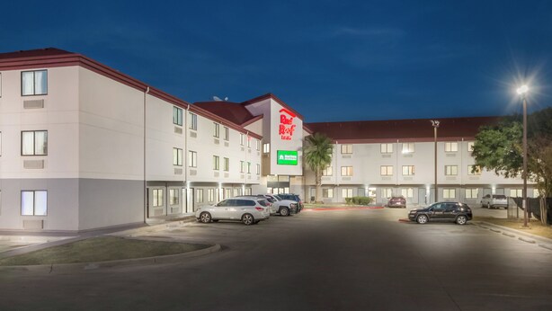 Un hotel de varios pisos, un estacionamiento con varios coches y un llamativo letrero de Red Roof Inn.