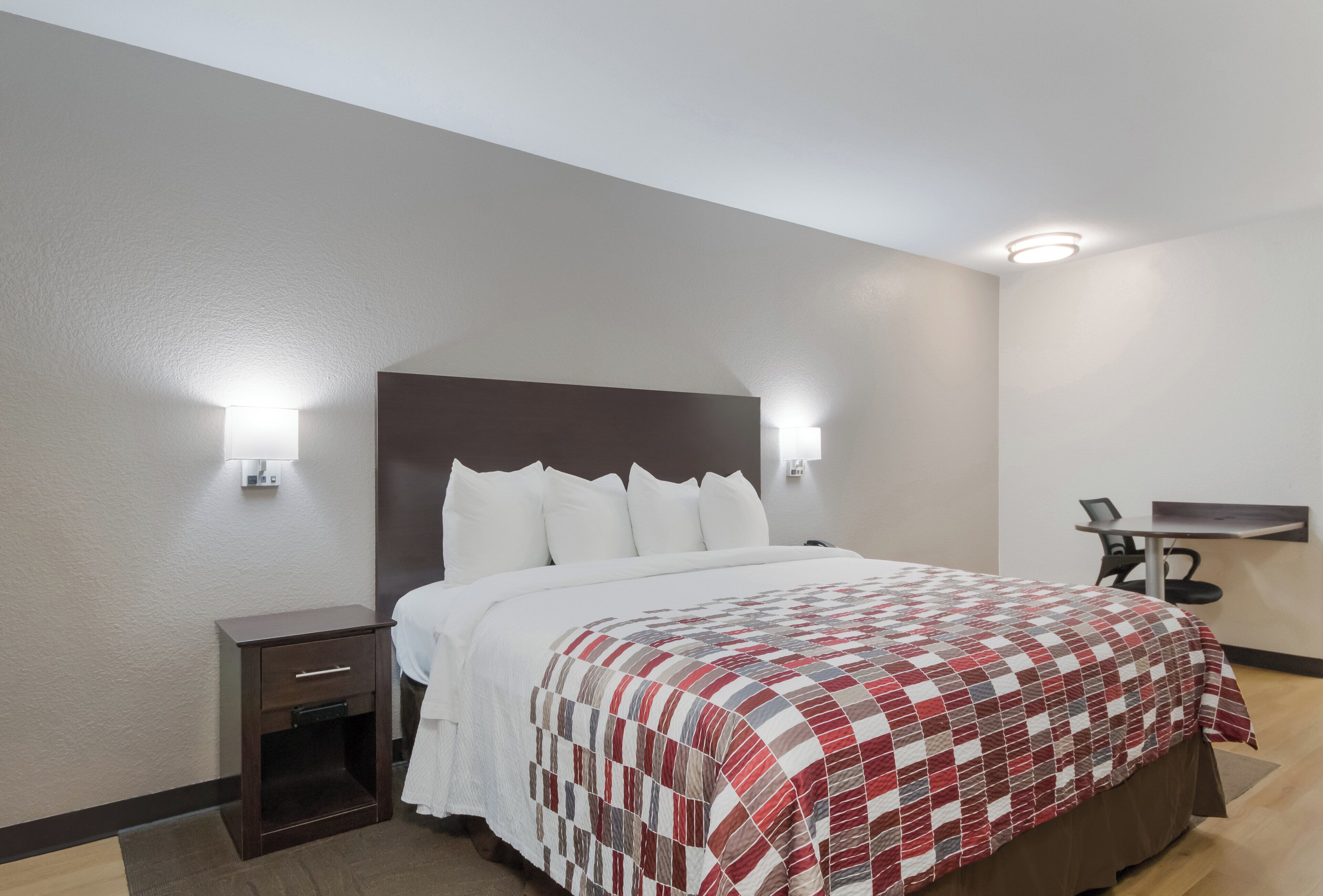 Habitación de hotel con cama, mesita de noche, lámpara y escritorio con silla.