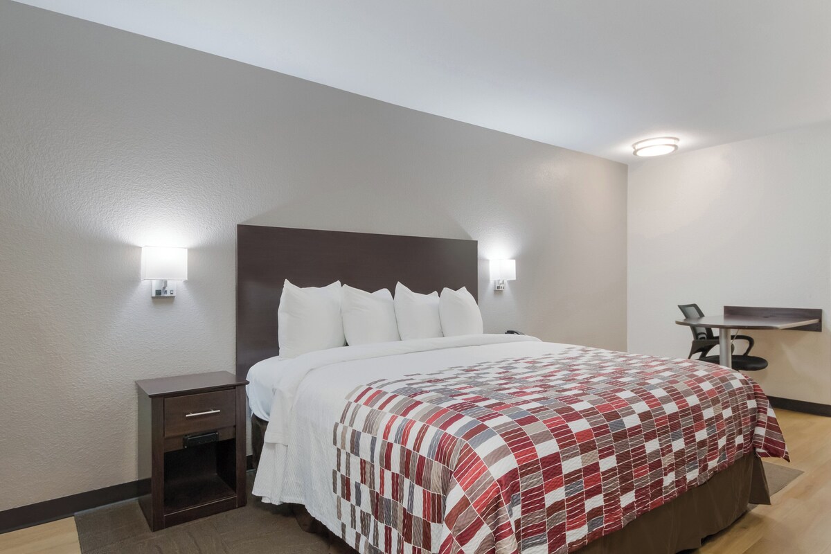 A hotel room with a bed, bedside table, lamp, and a desk with a chair.