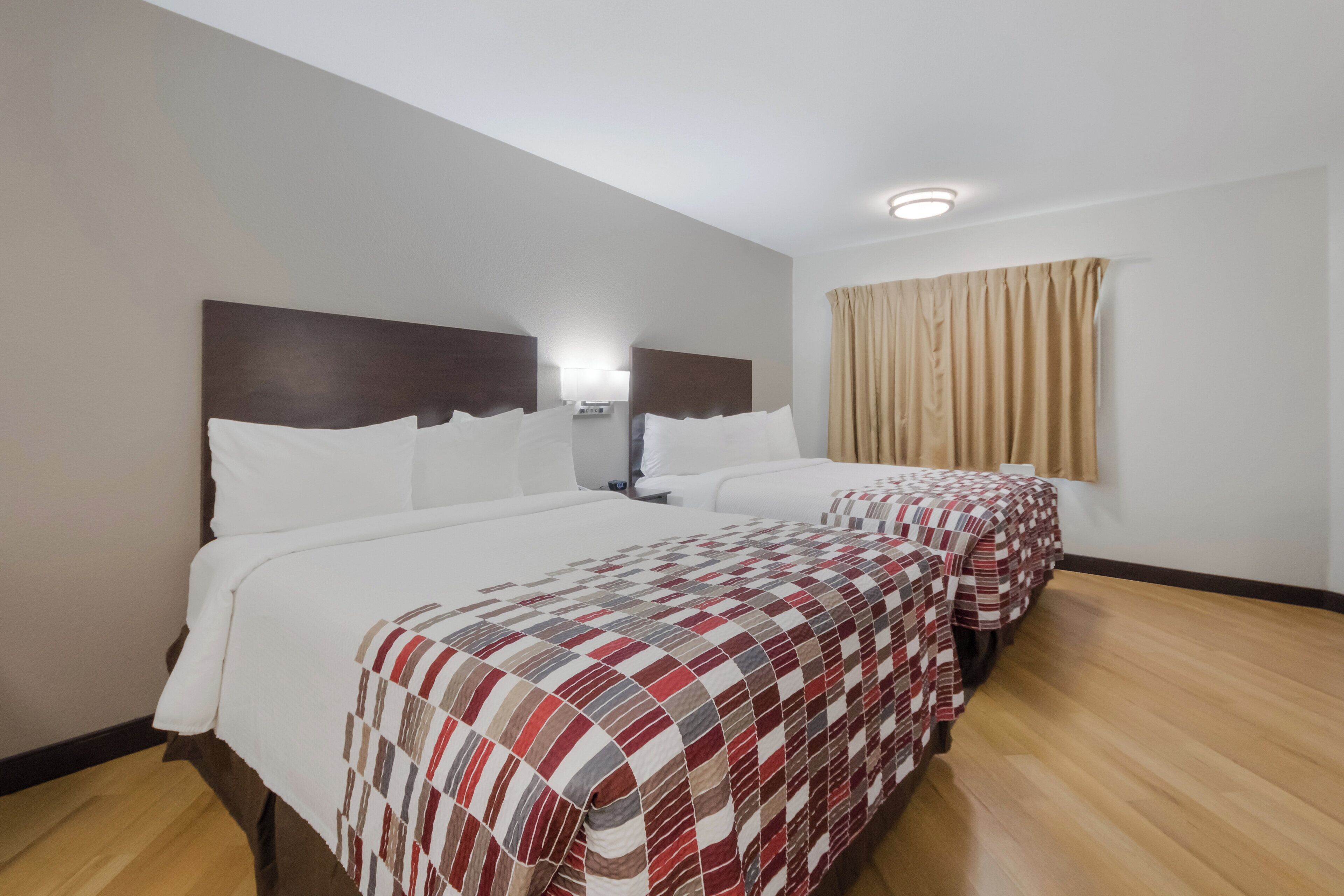 A hotel room with two beds, a nightstand, a lamp, and a window with curtains.
