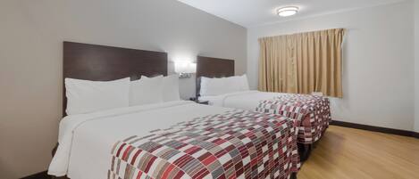 A hotel room with two beds, a nightstand, a lamp, and a window with curtains.