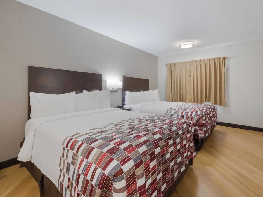 Habitación de hotel con dos camas, una mesita de noche, una lámpara y un ventanal con cortinas.