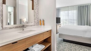 Habitación de hotel con tocador blanco, un espejo grande, un armario de madera y una cama con cubrecama blanco.