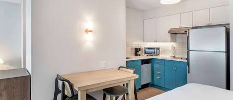 Kompakti hotellihuone, jossa on sänky, pieni pöytä tuoleineen, minikeittiö, jossa on mikroaaltouuni, sekä jääkaappi.