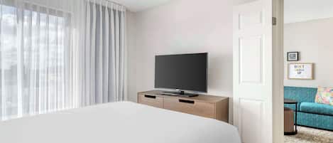 A hotel room with a bed, a TV on a wooden dresser, a door leading to another room, and a framed motivational quote on the wall.