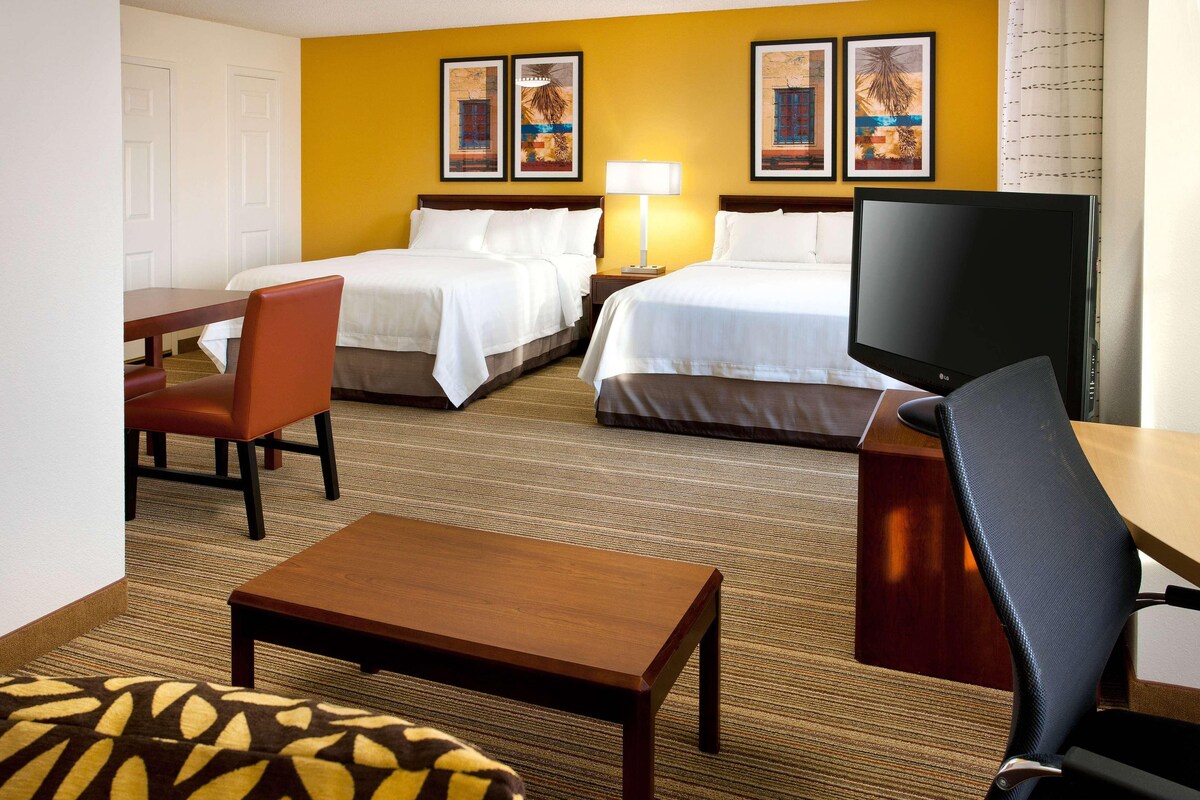 A hotel room with two beds, a TV, a desk, and a chair.