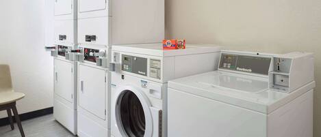 A laundry area with multiple white appliances, including a front-loading washer and dryer, and a stacked dryer unit.