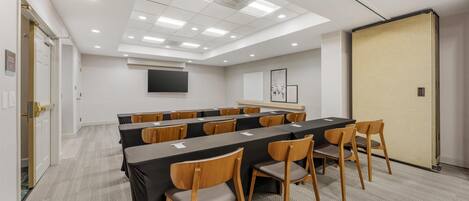 A conference room with a long table, wooden chairs, and a projector screen on the wall.