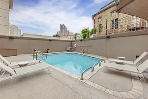 A rooftop pool area with lounge chairs, a pool table, and a view of the cityscape.