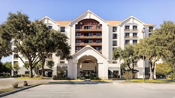 A multi-story hotel with a central entrance, balconies, and a clear sky.